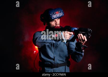 Young male wearing special devices for virtual reality games, isolated over red smoky background. Hi-tech Stock Photo