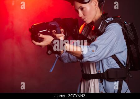 Shooting games, woman in special clothes wearing equipment, headsets and vr weapon. Background neon red backlit. Future innovations, modern technologi Stock Photo