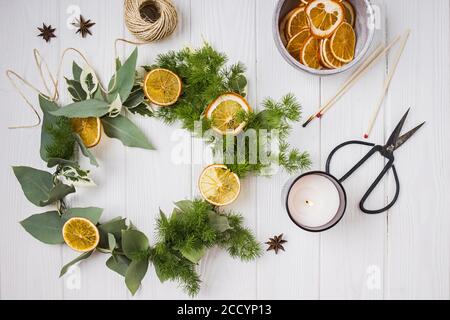 Hand made christmas wreath decorated with dry oranges on white table Stock Photo
