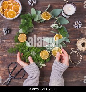 Woman's hands holding hand made Christmas wreath on wooden table Stock Photo