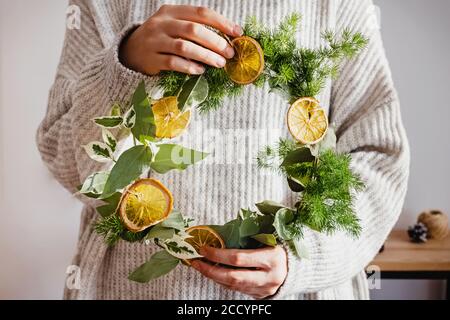 Woman in knitted sweater holding a hand made Christmas wreath. Stock Photo