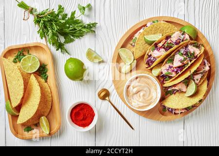 salmon tacos with shredded red cabbage salad with spicy yogurt sauce sprinkled with finely chopped parsley served on a bamboo plate on a white wooden Stock Photo