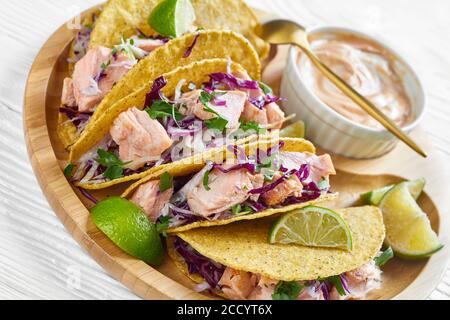 close-up of salmon tacos with red cabbage salad with spicy yogurt sauce sprinkled with finely chopped parsley served on a bamboo plate on a white wood Stock Photo