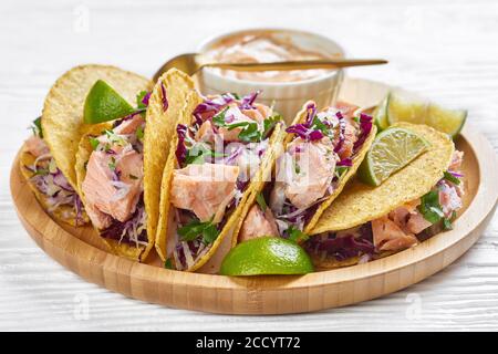 close-up of fish tacos with red cabbage salad with spicy yogurt sauce sprinkled with finely chopped parsley served on a bamboo plate on a white wooden Stock Photo