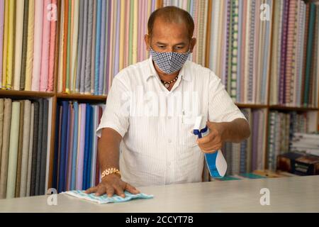 Shopkeeper in medical mask disinfecting table by using sanitizer - Cleaning dust on desk surface with cloth or Disinfectant Spray, to protect from Stock Photo