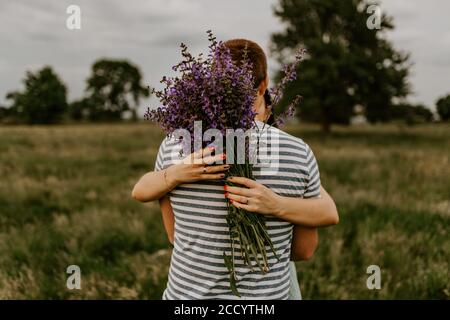 A brunette man in hugs a woman with bouquet of lilac and violet flowers Stock Photo