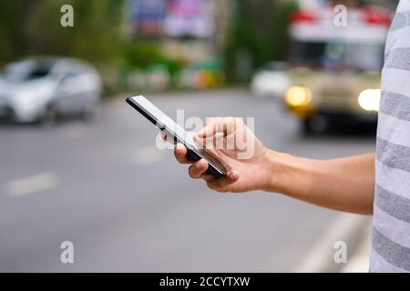 Hand of man using a mobile phone on the street. Use of transportation app. Stock Photo