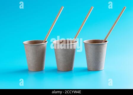 Three disposable brown craft paper cups with paper straws in a row on blue background. Eco-friendly tableware. Recycling concept. Zero waste theme Stock Photo