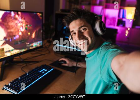 Image of caucasian cheerful man taking selfie photo while playing video game on computer at home Stock Photo