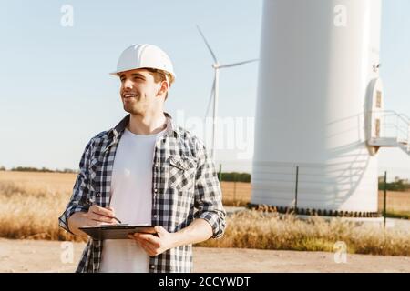An electrical engineer standing on a field with windmills, taking notes Stock Photo
