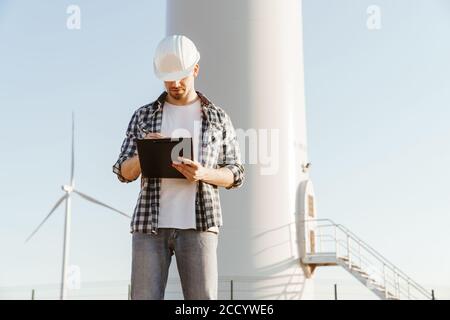 An electrical engineer standing on a field with windmills, taking notes Stock Photo