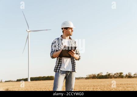 An electrical engineer standing on a field with windmills, taking notes Stock Photo