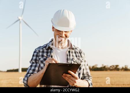 An electrical engineer standing on a field with windmills, taking notes Stock Photo