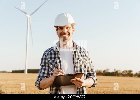 An electrical engineer standing on a field with windmills, taking notes Stock Photo
