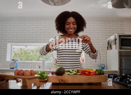 Smiling young woman food blogger clicking photo of chopped vegetables in kitchen counter using smartphone Stock Photo