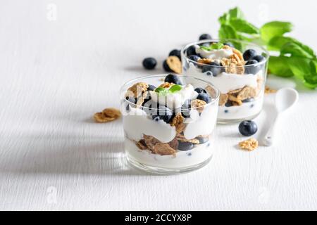 Homemade breakfast of muesli, yogurt and blueberries in glasses on the white. Helathy vegetarian eating. Stock Photo