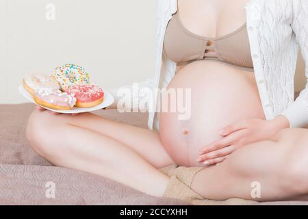 Close up of pregnant woman is eating many donuts relaxing in bed. Unhealthy dieting during pregnancy concept. Stock Photo