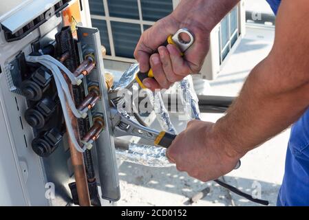 HVAC technician is working on air conditioner units on a roof of new industrial building.Technician hand using fix wrench to tighten outdoor unit of a Stock Photo