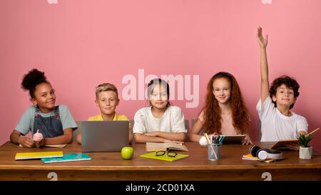 Smart Caucasian boy and his friends ready to answer lesson at table against pink background, copy space Stock Photo