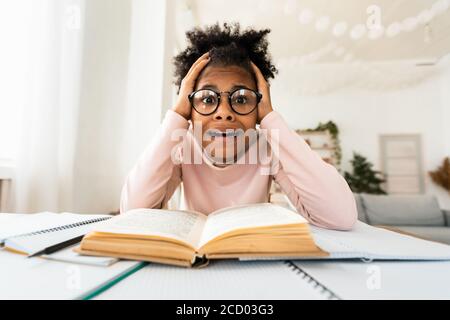 Unhappy Black Schoolgirl Looking At Camera Sitting At Books Indoor Stock Photo
