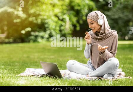 Happy muslim woman having video call on laptop at park Stock Photo