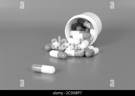 Closeup grayscale shot of medical capsules dropped out from the container Stock Photo