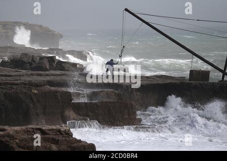 A man watches the waves crash against the shoreline at Portland Bill in Dorset. Stock Photo