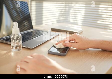 Close up pf female hands sanitizing smartphone while working at desk in post pandemic office, copy space Stock Photo