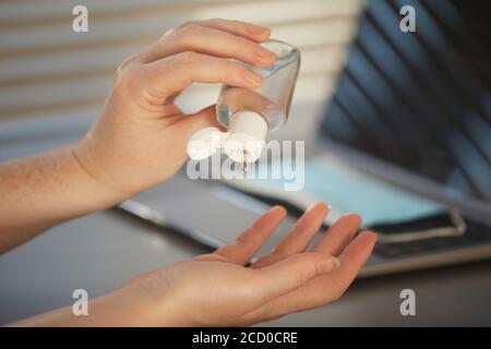 Closeup pf unrecognizable woman sanitizing hands with gel while working at desk in post pandemic office, copy space Stock Photo