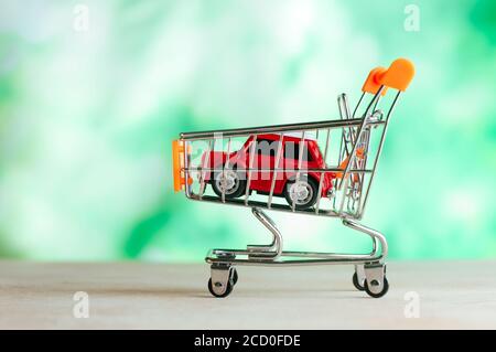 Car toy in small shopping cart over light green blur background with blank space for text. Stock Photo