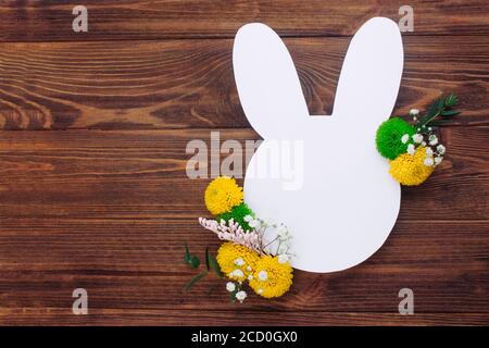Easter bunny from white paper with flowers on rustic wooden background with blank space for text. Top view, flat lay. Stock Photo