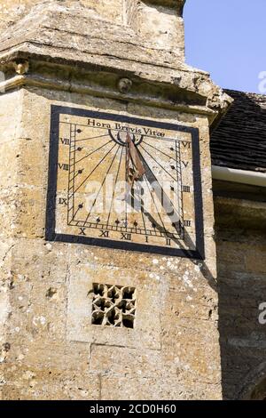The sundial with the motto Hora Brevis Vitae (the Hour of this Short Life) on the church of St Andrew in the Cotswold village of Chedworth, Gloucester Stock Photo