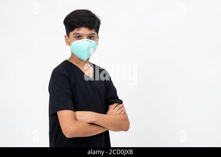 Young Indian boy wears face mask for protection against Covid-19. Cute teenager standing with arms crossed. Stock Photo