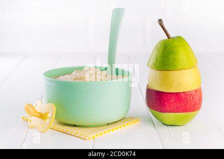 Natural baby food concept. Fruit puree in bowl near pyramid of apples and pear pieces on white background with blank space for text. Stock Photo