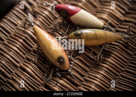 Examples of old South Bend fishing lures, or plugs, designed to catch predatory fish displayed on an old whicker tackle box. From a collection of vint Stock Photo