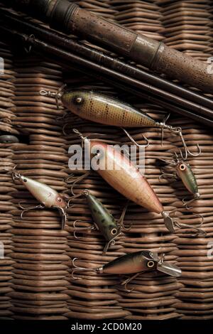 Examples of old South Bend fishing lures, or plugs, to catch predatory fish displayed on a whicker tackle box. The larger lures are South Bend Stock Photo