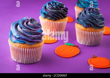 Halloween cupcakes with dark whipped cream on violet background with pumpkins. Selective focus. Stock Photo