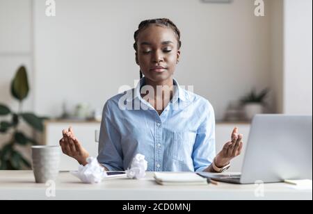 Coping With Stress At Work. Young African Businesswoman Meditating In Office Stock Photo