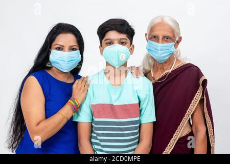 Indian grandmother, daughter and son wearing Covid-19 protection mask. Happy Indian family standing and looking into the camera