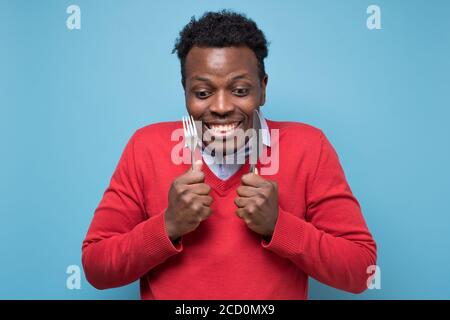 Hungry african man holding fork and knife raised waiting for dinner. Stock Photo