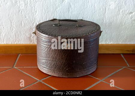 Vintage round suitcase lying on the floor on brown tiles against a white wall. Stock Photo