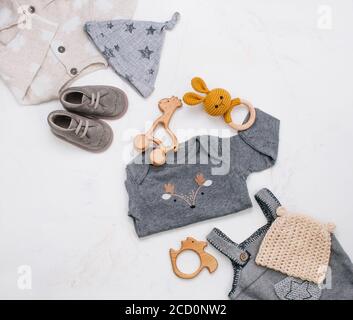 Newborn baby's clothing, wooden beanbag, teether and toy on light marble background with blank space for text. Top view, flat lay. Stock Photo