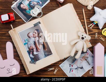 Open album with mother and baby picture near accessories on rustic wooden background. Blank space for text. Top view, flat lay Stock Photo