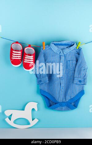 Red baby booties and blue body kit on clothespins over blue background with blank space for text. Stock Photo