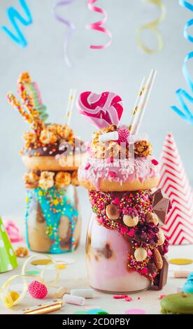 Kids party concept: Raspberry freak shake topping with donut and caramel popcorn and decorated with caramel and milk chocolate on party table; selecti Stock Photo