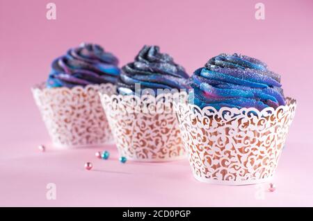 Three vanilla cupcakes with galaxy dark whipped cream in delicate paper wrapper on pink background Stock Photo