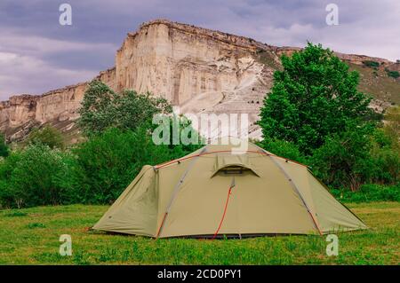 Tourist tent on the summer meadow in front of limestone mountain rocky cliff; selective focus Stock Photo