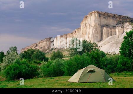 Tourist tent on the summer meadow in front of limestone mountain rocky cliff, selective focus Stock Photo