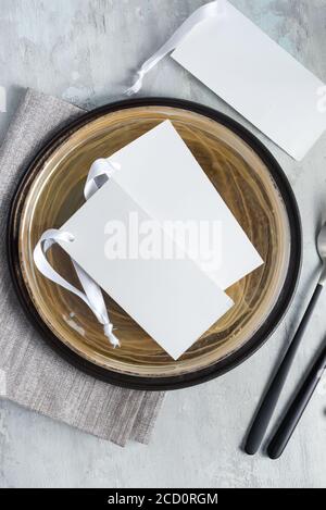Served ceramic plate with mock-up paper invitation cards or blank brochures with fresh tender tulip flowers on a light grey marble background, copy sp Stock Photo