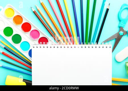 An album for creative development at school, with stationery on a cyanide background. A palette of colored paints, markers, brushes and pencils. Stock Photo